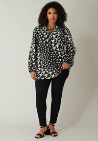Sort og hvidt houndstooth-mønsteret bluse med snorehals, oversized pasform og lange ærmer, parret med sorte skinny jeans og hæle.
