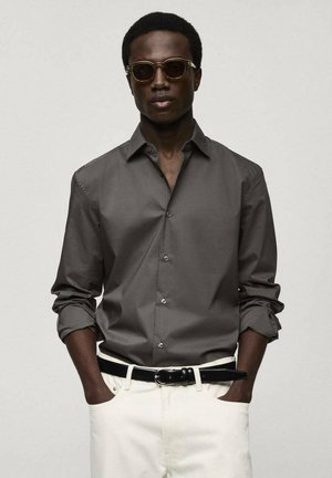 Dark gray button-up shirt with roll-up sleeves, black belt, and white pants. Sunglasses with gold-tone accents complete the look.
