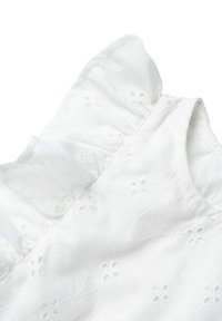 Blouse blanche en coton avec des épaules volantes, broderies florales et une texture légèrement transparente. Fini lisse, tissu léger.