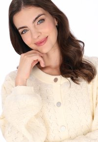 Jasnożółty sweter o splocie z teksturowanym wzorem zygzakowym, z prążkowanymi mankietami i trzema okrągłymi guzikami o lekkim połysku.