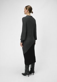 Abito lungo in maglia con una texture a coste, che passa da grigio scuro a nero, caratterizzato da maniche lunghe e una silhouette aderente.
