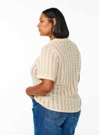 Bež värviga lühikeste varrukatega kootud särk struktureeritud kraega, millel on reljeefne mustriga ja lõdvestunud lõige, kombineeritud siniste teksapükstega.