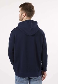 Sweatshirt à capuche bleu marine en tissu doux, doté d'une poche kangourou et d'un ourlet côtelé avec un discret logo sur la manche.