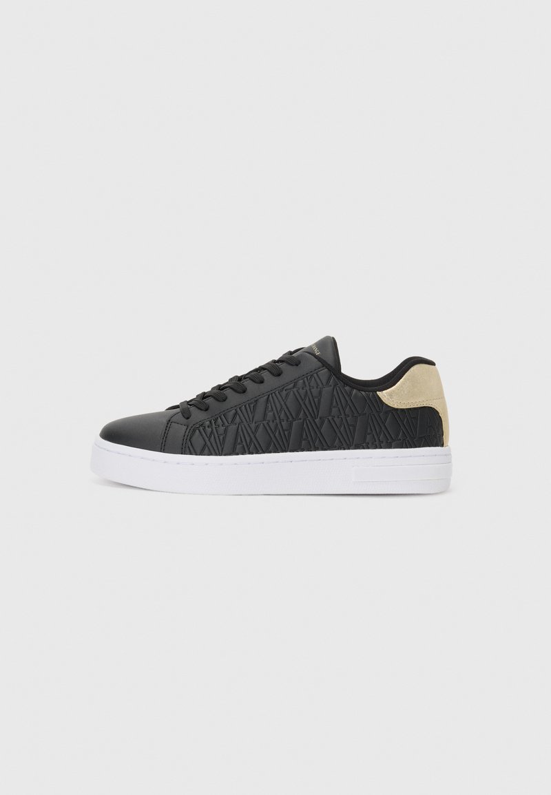 Svart sneaker med teksturert overdel som har geometriske mønstre, hvit mellomsåle og gulldetalj på hælen. Snørelukking. Flat såle.