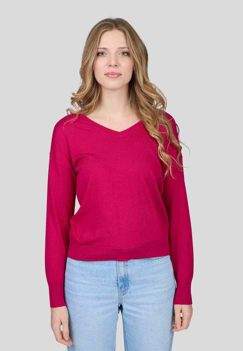 Pull à col en V de couleur rose vif, en tissu tricoté, coupe ample, manches longues, ourlet côtelé, associé à un jean bleu clair.