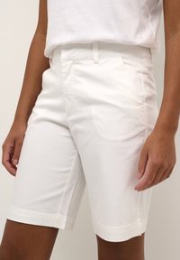 Shorts en coton blanc avec une texture lisse, dotés de poches latérales, d'une coupe classique et de bords bien cousus pour un look soigné.