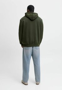 Olivengrøn hoodie med snoretræk i hætten, afslappet pasform og ribbede manchetter; parret med lyseblå straight-leg jeans og beige sko.