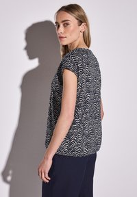 Maglietta a maniche corte a righe blu navy e crema, presenta un design a onde e una vestibilità comoda. Tessuto morbido, esposto su uno sfondo neutro.