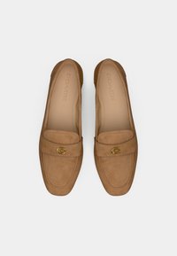Mocassini in suede marrone chiaro con punta arrotondata, dotati di una spilla in metallo dorato a forma di "C" e dettagli cuciti sulla parte superiore. Design con suola piatta.