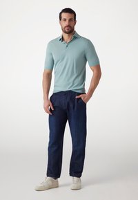 Gaiši zils īsa piedurkņu polo krekls apvienots ar tumši ziliem brīva piegriezuma biksēm un baltām kedām. Gluda tekstūra un klasiskā apkakles dizains.