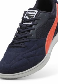 Zapatilla deportiva azul marino con tela texturizada, acentos naranjas y suela blanca. Presenta diseño de cordones y cuello acolchado para mayor comodidad.