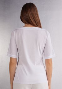 T-shirt bianco a maniche corte con vestibilità rilassata, in morbido cotone e scollatura tonda. Presenta le maniche arrotolate e una texture liscia.