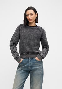 Mikina s okrúhlym výstrihom v tmavosivej farbe so vyblednutou textúrou, obsahujúca spevnené švy, kontrastné pruhy pozdĺž rukávov a rebrované manžety.