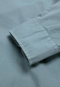 Tejido azul claro con costuras visibles y detalle de manga doblada sobre una superficie textil lisa.