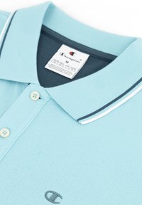 Jasnoniebieska koszulka polo z teksturowanym materiałem, szarym wnętrzem kołnierza oraz kontrastowymi białymi paskami. Wyposażona w trzy guziki i logo.