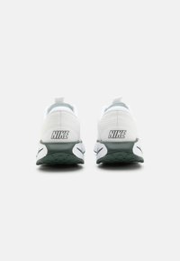 Hvite Nike-sneakers med teksturert overdel, grønne detaljer på sålen, og synlig merkevare på hælen og sidene.