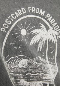 Camiseta gris con un diseño gráfico blanco que incluye un sol, palmeras, olas y montañas, etiquetado "POSTAL DEL PARADISO."