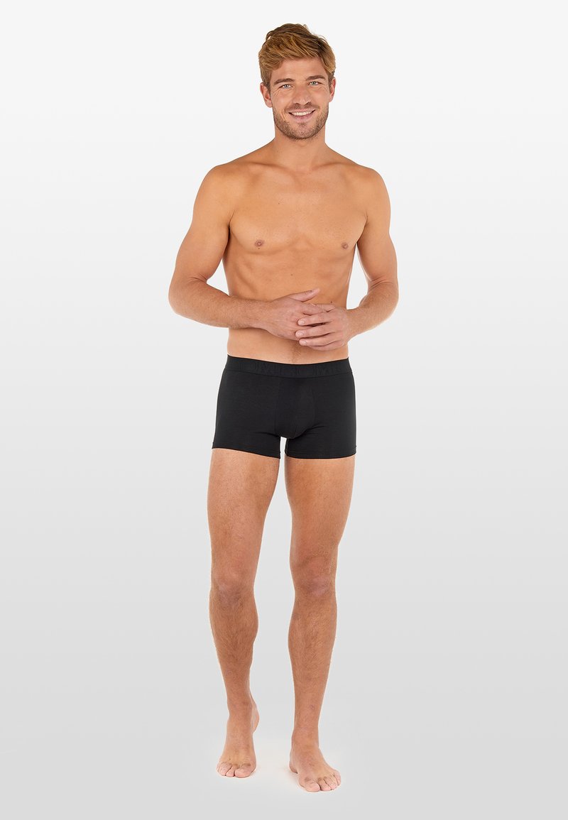 Svarta boxershorts med en figurnära design och elastisk midja, bärs av en stående manlig modell med bar hud, armarna avslappnat vid sidorna.