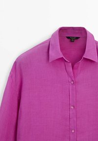 Camicia di lino rosa con collo a falde, chiusura a bottoni e maniche lunghe. Il tessuto presenta una consistenza liscia con una leggera lucentezza.
