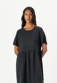 Schwarzes Kurzarmkleid mit Rundhalsausschnitt und gestuftem, gerafftem Oberteil. Weicher Stoff mit fließender Silhouette und subtiler Textur.