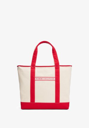 Canvas draagtas met rode straps en onderkant, voorzien van een centraal logo in rode draad. Rechthoekige vorm, versterkte naden.