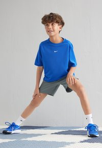 Blaues kurzärmliges Sportshirt mit Nike-Logo, kombiniert mit grauen Shorts. Blaue Sneakers und weiße Socken vervollständigen das sportliche Outfit.