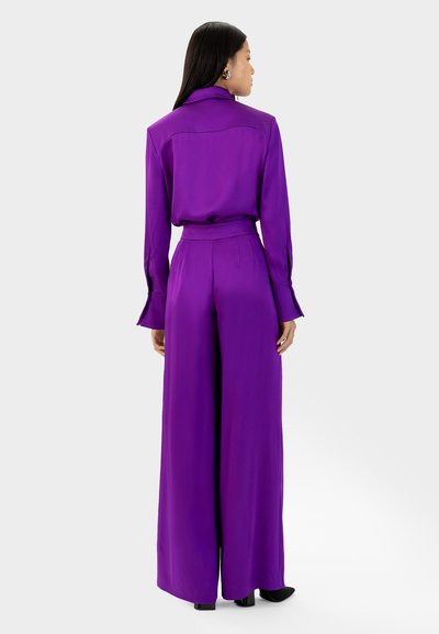 Paarse satijnen jumpsuit met lange mouwen, een kraag, een ceintuur in de taille en wijde pijpen. Gladde textuur en een op maat gemaakte pasvorm.