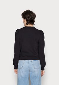 Svart sweatshirt med puffärmar, figursydd midja och mjuk textur. Bärs med ljusblå, högmidjade, slitna jeans.