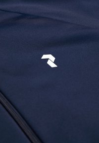 Tejido azul marino con una textura suave, que presenta un logo geométrico blanco y una cremallera visible a lo largo del borde.