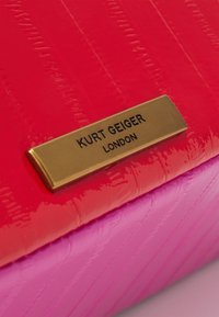 Punainen ja vaaleanpunainen tekonahkainen kirjekuorilaukku krokotiilinkuviolla ja kultaisen värisellä metallisella merkkipohjalla, jossa lukee "Kurt Geiger London".