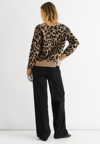 Knit sweater in tan with a black leopard print, featuring a loose fit, crew neckline, and ribbed cuffs. Paired with wide black pants.