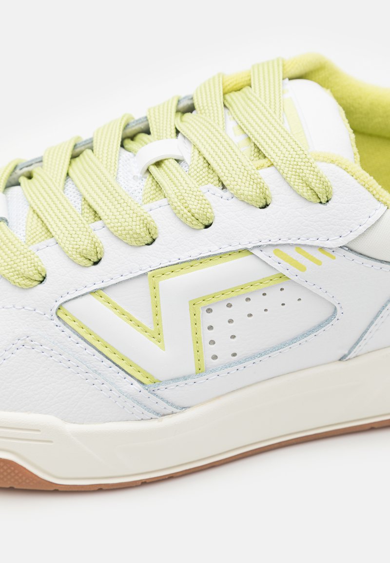 Zapatilla blanca con acentos en verde claro y detalles decorativos. Cuenta con cordones texturizados y una suela de goma, destacando un diseño deportivo.