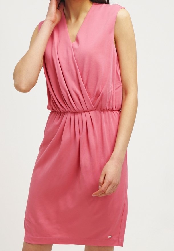 Mouwloze roze jurk tot op de knie met een V-hals wikkelbovenstuk en een geplooide taille, gedragen door een vrouw tegen een effen achtergrond.