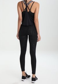 Canottiera atletica nera con spalline incrociate e leggings neri con un sottile motivo a leopardato. Entrambi sono aderenti ed elasticizzati.