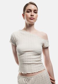 Off-shoulder cremetop med tekstureret stof, korte ærmer og bølget kant, parret med matchende bund. Glat, let materiale.