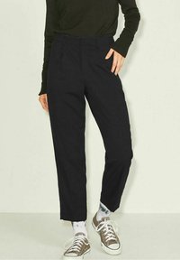 Svarta skräddarsydda byxor med rak skärning, med framfickor och en slät yta. Bärs med avslappnade sneakers och mönstrade strumpor.