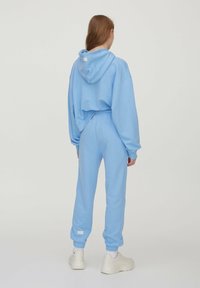 Helles blauer Sweatshirt und passende Sweatpants, beide aus weichem Stoff gefertigt. Verfügt über eine Kapuze, elastische Bündchen und ein kleines Logoschild an den Hosen.