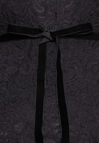 Melna mežģīņu augšdaļa ar ziedu rakstu un teksturētu apdari. Ietver melnu satīna jostu, kas piešķir kontrastu dizainam.