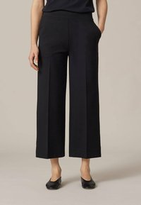 Svarta vida byxor med en slät textur, med sidofickor och en skräddarsydd passform. Avslutade med en ren fåll vid ankeln.