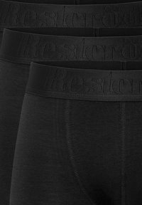 Schwarze Boxershorts aus Baumwolle mit einem elastischen Bund, der mit "Resteröd" geprägt ist. Der Stoff erscheint glatt mit einem matten Finish. Mehrere Paare übereinander gestapelt.