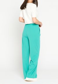 Turquoise wide-leg pants with an elastic waistband and side pockets, made from a smooth, lightweight fabric. Back view shown.