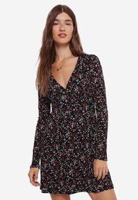 Svart långärmad klänning med blommönster i röd, vit och grön. V-ringning och utsvängd silhuett. Mjuk tygkvalitet.