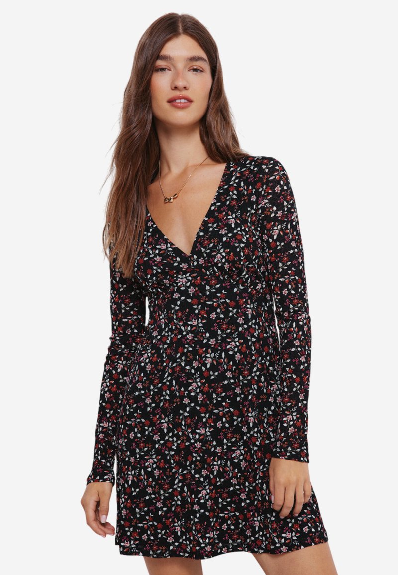 Svart långärmad klänning med blommönster i röd, vit och grön. V-ringning och utsvängd silhuett. Mjuk tygkvalitet.