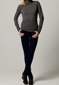 Maglione grigio a collo alto abbinato a jeans skinny blu scuro e stivaletti. Il maglione ha un design aderente con maniche lunghe e una texture liscia.