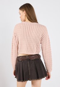 Heklet rosa genser med lange ermer, sammen med et mørkt denimskjørt med plisseringer og et dekorativt flettet belte.