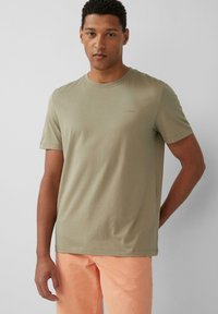 Olive zielona bawełniana koszulka z okrągłym dekoltem, krótkimi rękawami i subtelnym logo na klatce piersiowej, zestawiona z jasnopomarańczowymi spodniami.