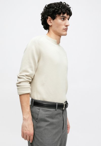 Μπεζ πλεκτό πουλόβερ με στρογγυλή λαιμόκοψη και γυρισμένα μανίκια, συνδυασμένο με γκρι ραμμένο παντελόνι και μαύρη ζώνη με λευκές ραφές.