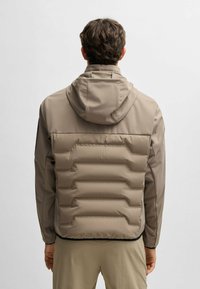 Ljusbrun pufferjacka med huva, med en slät ovandel och quiltad nederdel, visad från baksidan.