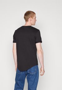 Black short-sleeve t-shirt with a crew neckline and rolled cuffs, made of smooth fabric, worn with blue denim jeans.