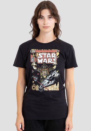 Junge Frau trägt ein schwarzes Star Wars T-Shirt mit Darth Vader, einem Raumschiff und Retro-Comic-Grafiken auf grauem Hintergrund.